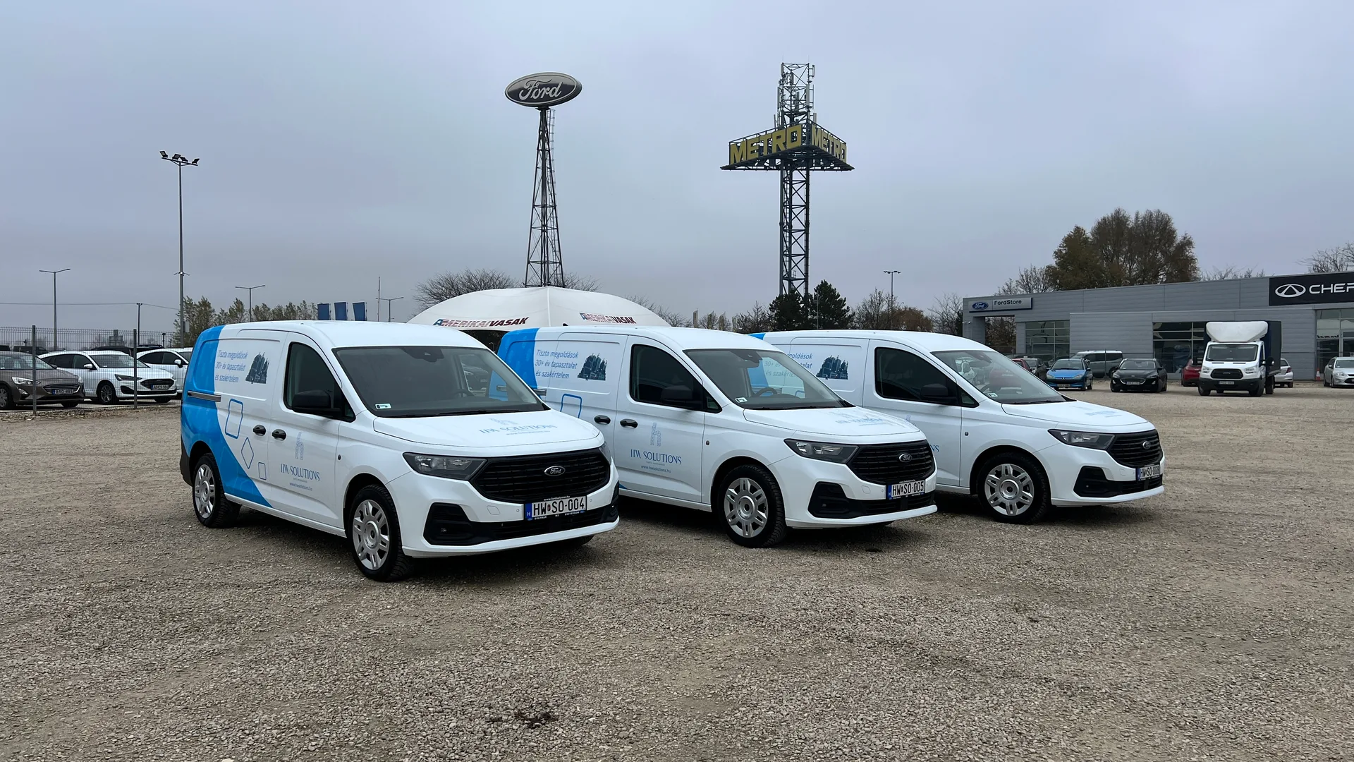 HW Solutions Ford Transit Connect flotta – három fehér Transit Connect Van egységes kék arculati grafikával a Ford márkakereskedés előtt